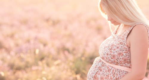 Understanding the motivations of surrogates in the UK - a pregnant person stands in a field of pink flowers